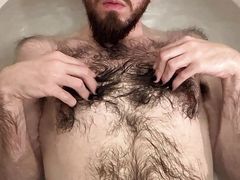 Skinny bald white otter with bright blue eyes and black painted nails showing off very hairy body in the bathtub